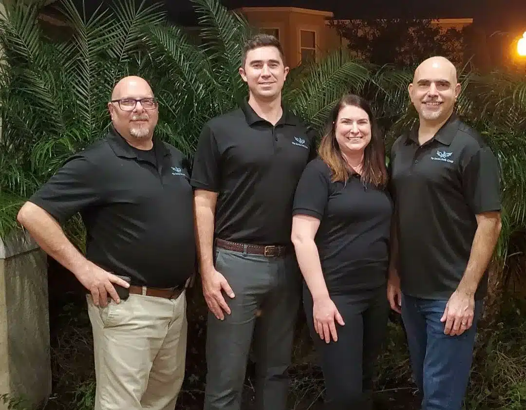 The Service Profit Group's employees, standing in black SPG polo shirts smiling, shown from the knee up in a knock-out photo with no background, From left to right, Director of Awesomeness, Joe O'Grady, Senior consultant Drew Melamed, consultant Alison Tawney, consultant Darren George, and Director of Operations Phil Denato